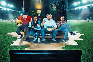 Image showing Ardent fans are sitting on the sofa and watching TV in the middle of a football field.