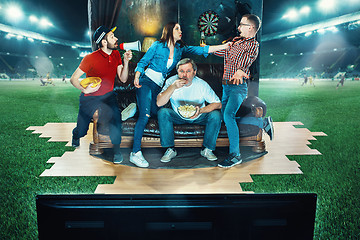 Image showing Ardent fans are sitting on the sofa and watching TV in the middle of a football field.