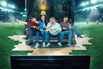 Image showing Ardent fans are sitting on the sofa and watching TV in the middle of a football field.