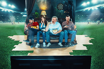 Image showing Ardent fans are sitting on the sofa and watching TV in the middle of a football field.