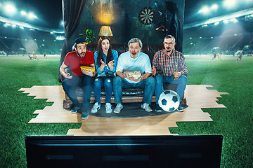 Image showing Ardent fans are sitting on the sofa and watching TV in the middle of a football field.