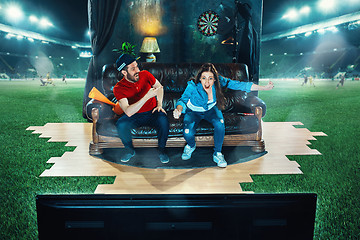 Image showing Ardent fans are sitting on the sofa and watching TV in the middle of a football field.