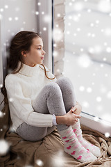 Image showing sad girl sitting on sill at home window in winter