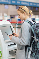 Image showing Casual caucasian woman using smart phone application and check-in machine at the airport getting the boarding pass.