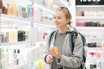 Image showing Blond young female traveler wearing travel backpack choosing perfume in airport duty free store.