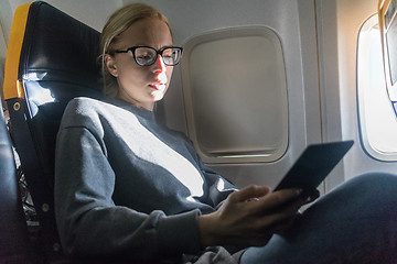 Image showing Woman wearing glasses reading on digital e-reader while traveling by airplane.