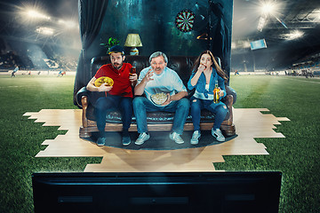 Image showing Ardent fans are sitting on the sofa and watching TV in the middle of a football field.
