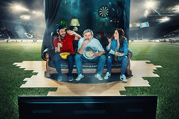 Image showing Ardent fans are sitting on the sofa and watching TV in the middle of a football field.