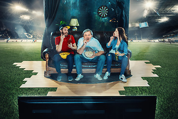 Image showing Ardent fans are sitting on the sofa and watching TV in the middle of a football field.