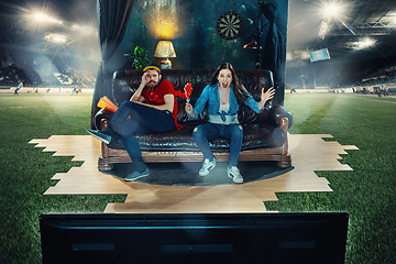 Image showing Ardent fans are sitting on the sofa and watching TV in the middle of a football field.