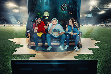 Image showing Ardent fans are sitting on the sofa and watching TV in the middle of a football field.