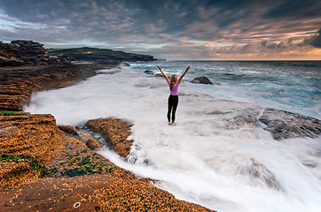 Image showing Girl standing on rocks as ocean waves wash past her feet