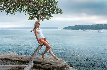 Image showing Female sitting by the seashore on the curved trunk of a tree