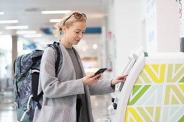 Image showing Casual caucasian woman using smart phone application and check-in machine at the airport getting the boarding pass.