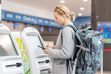 Image showing Casual caucasian woman using smart phone application and check-in machine at the airport getting the boarding pass.