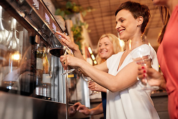 Image showing happy women pouring wine from dispenser at bar