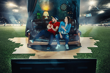 Image showing Ardent fans are sitting on the sofa and watching TV in the middle of a football field.