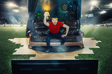 Image showing Male fan sitting on the sofa and watching TV in the middle of a football field.