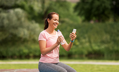 Image showing woman with smartphone drinking water in park