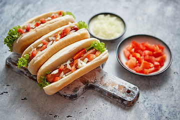 Image showing Three barbecue grilled hot dogs with sausage placed on wooden cutting board