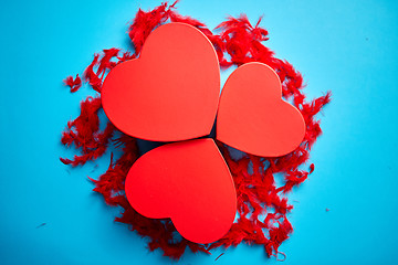 Image showing Three red, heart shaped gift boxes placed on blue background among red feathers