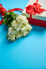 Image showing Bouquet of white roses with red bow on blue background. Boxed gift on side