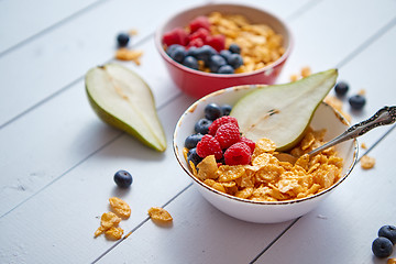 Image showing Golden cornflakes with fresh fruits of raspberries, blueberries and pear in ceramic bowl