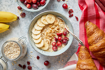 Image showing Ceramic bowl of oatmeal porridge with banana, fresh cranberries and walnuts