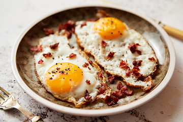 Image showing Two fresh fried eggs with crunchy crisp bacon served on rustic plate