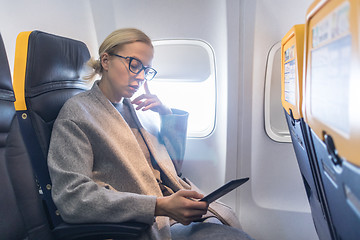 Image showing Woman wearing glasses reading on digital e-reader while traveling by airplane.