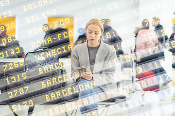 Image showing Female traveler using her cell phone while waiting to board a plane at departure gates at airport terminal.