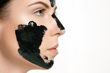 Image showing Young beautiful woman applying a mask for the face of the therapeutic black mud. Spa treatment