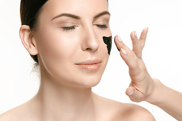 Image showing Young beautiful woman applying a mask for the face of the therapeutic black mud. Spa treatment