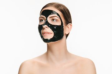 Image showing Young beautiful woman applying a mask for the face of the therapeutic black mud. Spa treatment