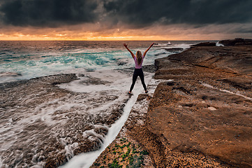 Image showing Spirited girl standing over rock crevice as waves wash in