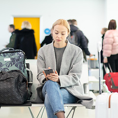 Image showing Female traveler using her cell phone while waiting to board a plane at departure gates at airport terminal.