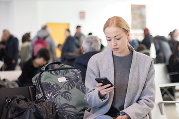 Image showing Female traveler reading on her cell phone while waiting to board a plane at departure gates at airport terminal.