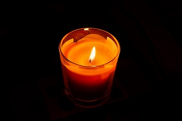 Image showing A bright orange candle burning in the dark