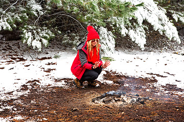 Image showing Girl crouching and warming frost bite hands in the smouldering fire