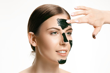 Image showing Young beautiful woman applying a mask for the face of the therapeutic black mud. Spa treatment