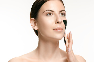 Image showing Young beautiful woman applying a mask for the face of the therapeutic black mud. Spa treatment