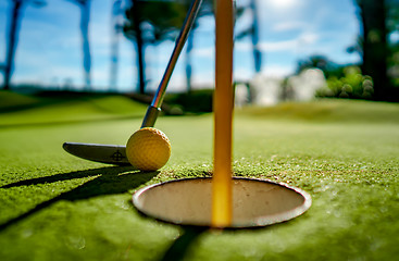Image showing Mini Golf yellow ball with a bat near the hole at sunset