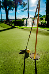 Image showing Mini Golf yellow ball with a bat near the hole at sunset