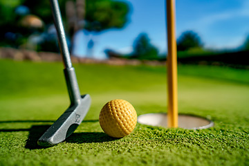 Image showing Mini Golf yellow ball with a bat near the hole at sunset