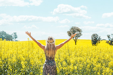 Image showing Woman in dress arms in the air standing in front of olden canola fields