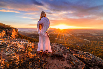 Image showing Angelic woman with angel wings and white dress on mountain cliffs sunset