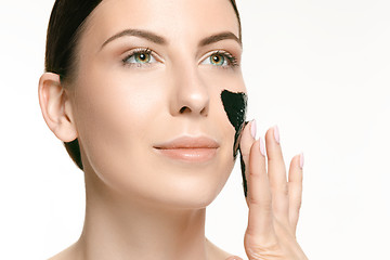 Image showing Young beautiful woman applying a mask for the face of the therapeutic black mud. Spa treatment