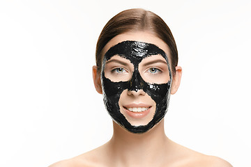 Image showing Young beautiful woman applying a mask for the face of the therapeutic black mud. Spa treatment