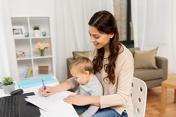 Image showing happy mother with baby and papers working at home