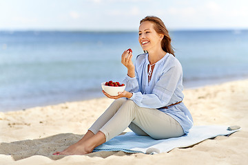 Image showing happy woman eating strawberries on summer beach
